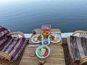 a table with plates of food on it next to the water at Nile Bride in Aswan