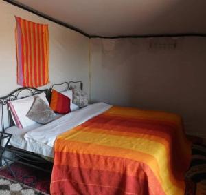 ein Schlafzimmer mit einem Bett mit bunten Laken und Kissen in der Unterkunft Excursion Erg chegaga in M’hamid El Ghizlane