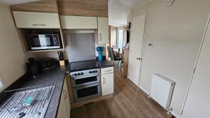 a small kitchen with a stove and a microwave at Great Yarmouth 10 Berth KP Holiday Home - NOW with Linen in Corton