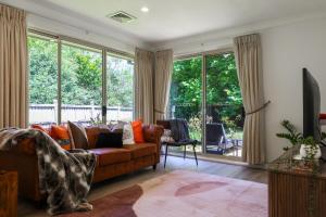 a living room with a brown couch and windows at Linden Getaway Bowral in Bowral