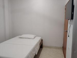 a small white room with a bed and a television at GTH Hostal in Arboletes