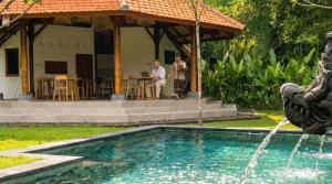 two people sitting in front of a house with a swimming pool at Sananda Aryani in Lovina