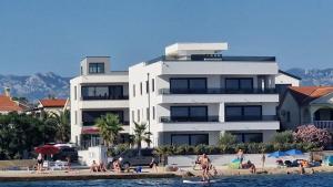 a large white building next to a beach with people at Dinary Apartman in Vir