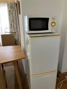 a microwave on top of a refrigerator next to a table at Green House Tsukuba Studio in Tsukuba
