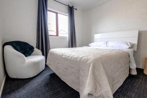 a bedroom with a white bed and a chair at Clock Tower Accommodation in Hokitika