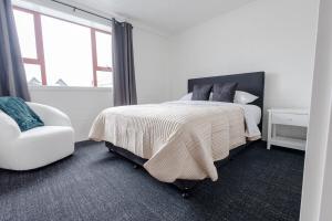 a white bedroom with a bed and a chair at Clock Tower Accommodation in Hokitika
