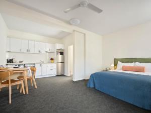 a bedroom with a bed and a table and a kitchen at Baileys Parkside Motel by VetroBlu in Perth