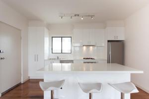 a white kitchen with a counter and two stools at St Kilda absolute beachfront views in Melbourne