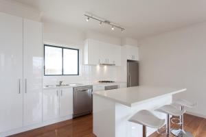 a white kitchen with a counter and stools in it at St Kilda absolute beachfront views in Melbourne +24 photos