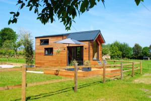 a small wooden cabin with an umbrella in a field at Tiny House - La P'tite Georgette in Canouville +10 photos