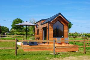 a small wooden cabin with an umbrella in a field at Tiny House - La P'tite Georgette in Canouville