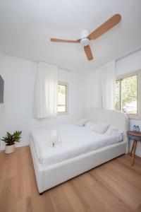 a white bedroom with a white bed and a ceiling fan at R26-Boutique in Zikhron Ya'akov