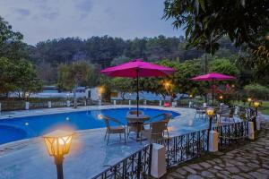 a pool with tables and chairs and umbrellas at Tripp Jim Corbett A River Access Resort in Marchula
