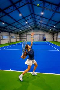 a woman serving a tennis ball on a tennis court at Hotel Wiki Sanok Events & Bowling in Sanok