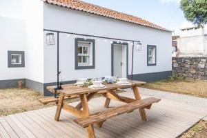a wooden picnic table in front of a white house at Grão de Areia - Mosteiros - 50m da praia - piscina privada in Mosteiros