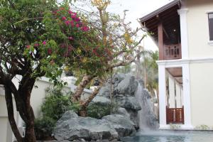 a waterfall in front of a house with a tree and pink flowers at Lux Hotel in Luang Prabang