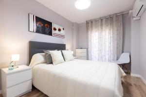 a white bedroom with a white bed and a chair at FORMENTOR Apartment in Salou