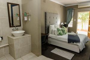 a bedroom with a bed and a sink and a mirror at St Andrews exclusive guesthouse in Klerksdorp +53 photos