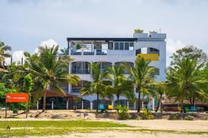 a building on the beach with palm trees in front at Monkey Tribe Alleppey in Alleppey