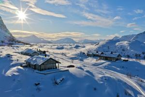 a village in the snow with the sun in the background at Lofoten Links Lodges in Gimsøy