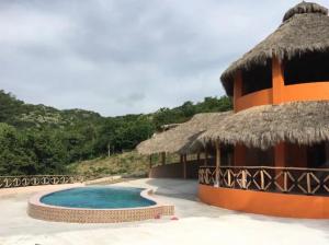 a building with a swimming pool and a thatch roof at Las Casitas de La Bahia Calechosa in Emiliano Zapata