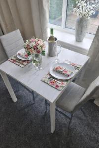 a white table with plates and glasses and flowers on it at Plum Cottage in Keswick