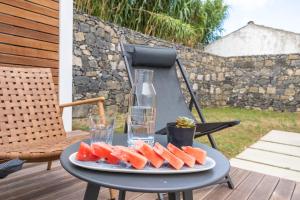 a plate of watermelon on a table with a bottle and glasses at Grão de Areia - Mosteiros - 50m da praia - piscina privada in Mosteiros