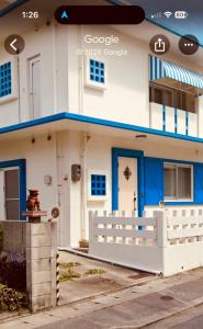 a white house with blue trim and a fence at 浦添民泊ejuイージュ in Urazoe