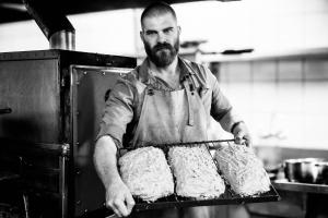 a man in a kitchen holding a tray of bread at Afrique Boutique Hotel O.R. Tambo in Boksburg