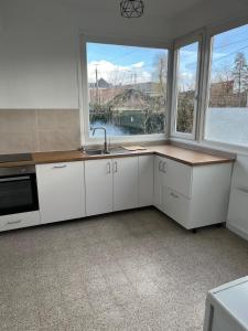 a kitchen with white cabinets and a sink and two windows at Maison Solesmes nord in Solesmes