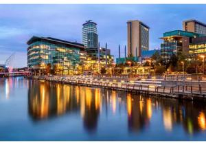 a city skyline with buildings and a river at night at 2 Bedroom APARTMENT in Manchester