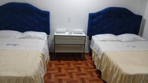 a room with two beds and a night stand with a bedskirts at Hotel Diamante Azul in Huancayo