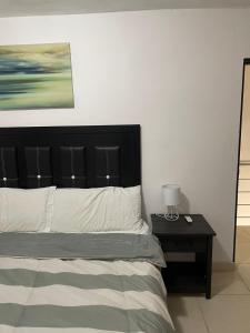 a bed with a black headboard and a table with a lamp at Casa Perfectamente Ubicada in Tampico
