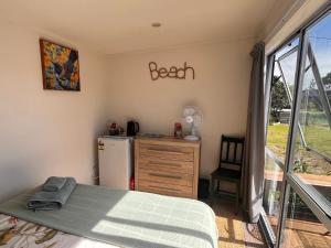 a bedroom with a bed and a refrigerator in it at Sunsets on Harbour Kauri or Totara Cabin in Matarangi +11 photos