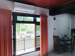 a room with a window with orange curtains and a table at Vihen Homestay in Dickwella