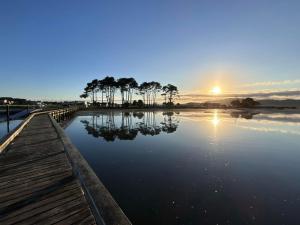 a sunset over a lake with trees and a dock at Sunsets on Harbour Kauri or Totara Cabin in Matarangi