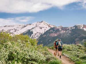 two people and a dog walking down a trail with mountains at Aspenwood - CoralTree Residence Collection in Snowmass Village