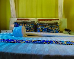 a bed with blue sheets and colorful pillows on it at Meltonia Luxury Inn in Busia +39 photos