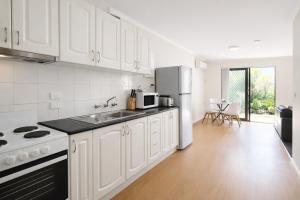 a white kitchen with a sink and a refrigerator at Beachside Garden Apt Beach Scarborough with Parking in Perth