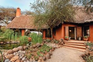 a small house with a thatch roof and a pond at Tawi Lodge in Amboseli