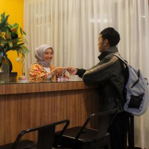 a man shaking hands with a woman at a counter at Hotel Indria in Bukittinggi