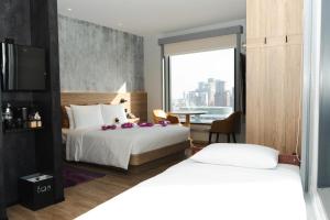 a hotel room with two beds and a table with a view at Moxy Bangkok Ratchaprasong in Bangkok