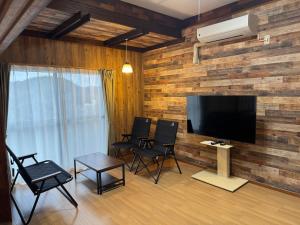 a living room with chairs and a television on a wooden wall at ぺろんち in Shinkamigoto
