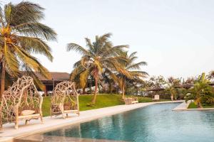 a swimming pool with two chairs and palm trees at Adouna Bay in Cap Skirring
