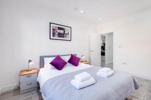 a white bedroom with a large bed with purple pillows at Luxurious 1 Bed Serviced Apartment with Wi-Fi in Corby