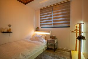 a bedroom with a bed with a nightstand and a window at Joohane Jejudo House in Jeju