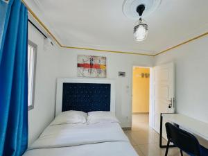 a bedroom with a bed and a desk with a blue curtain at CAMERHOME Banque SCB Cité des palmiers in Douala