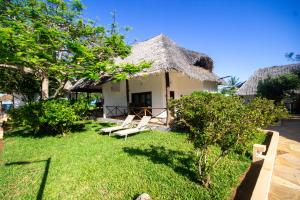 a house with a thatched roof and chairs in the yard at Reef & Beach Resort - Spa Jambiani in Jambiani