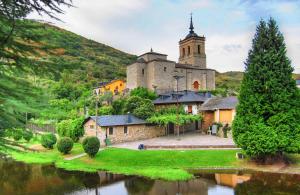 an old building with a church next to a river at Hostal El Horno in Molinaseca