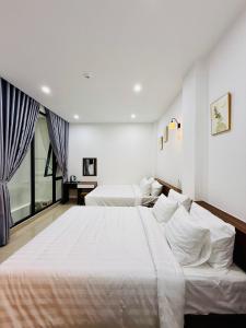 a white bedroom with two beds and a window at Amazon Hotel in Phước Hậu (1)